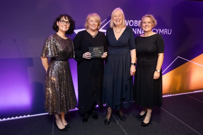 A group of four smiling on stage holding an awards plaque.