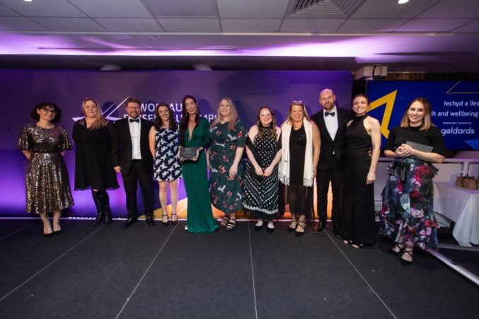 A group of eleven people standing on a stage at the Welsh Charity Awards. One person near the center is holding an award plaque.