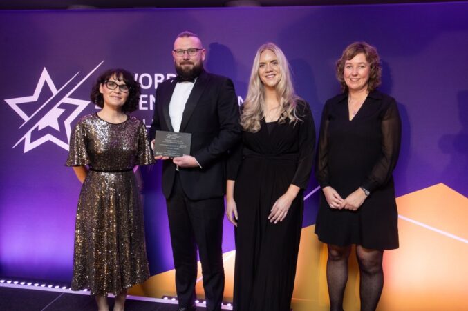 A group of four people standing on a stage at the Welsh Charity Awards. One person in the center is holding an award plaque.